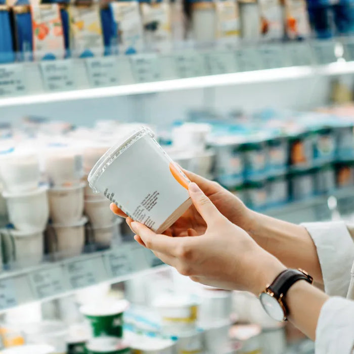 Consommatrice tenant un produit au rayon frais, en train de lire l’étiquette alimentaire dans un supermarché