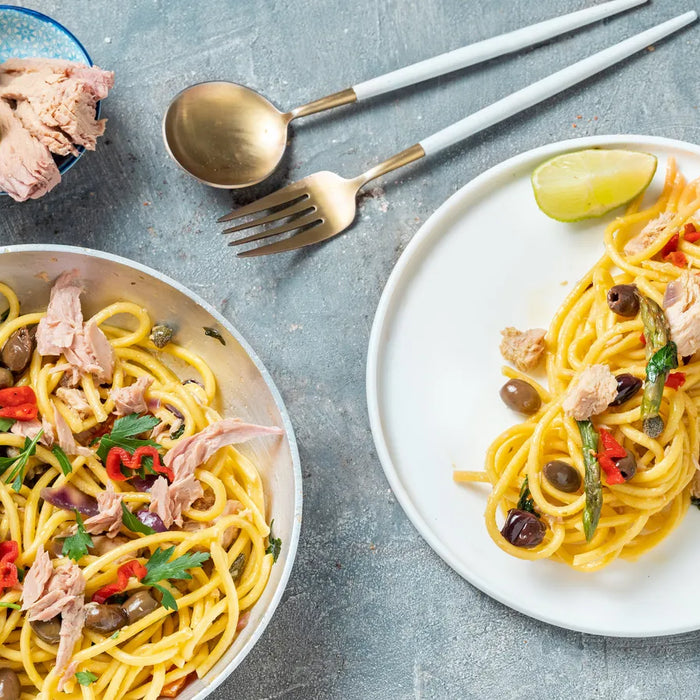 Pasta al tonno dans une poêle et une assiette avec thon, olives, piments et citron vert