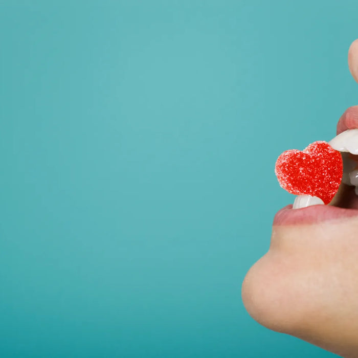Femme croquant une sucrerie en forme de cœur, symbole de l'impact de l'alimentation sur la santé dentaire