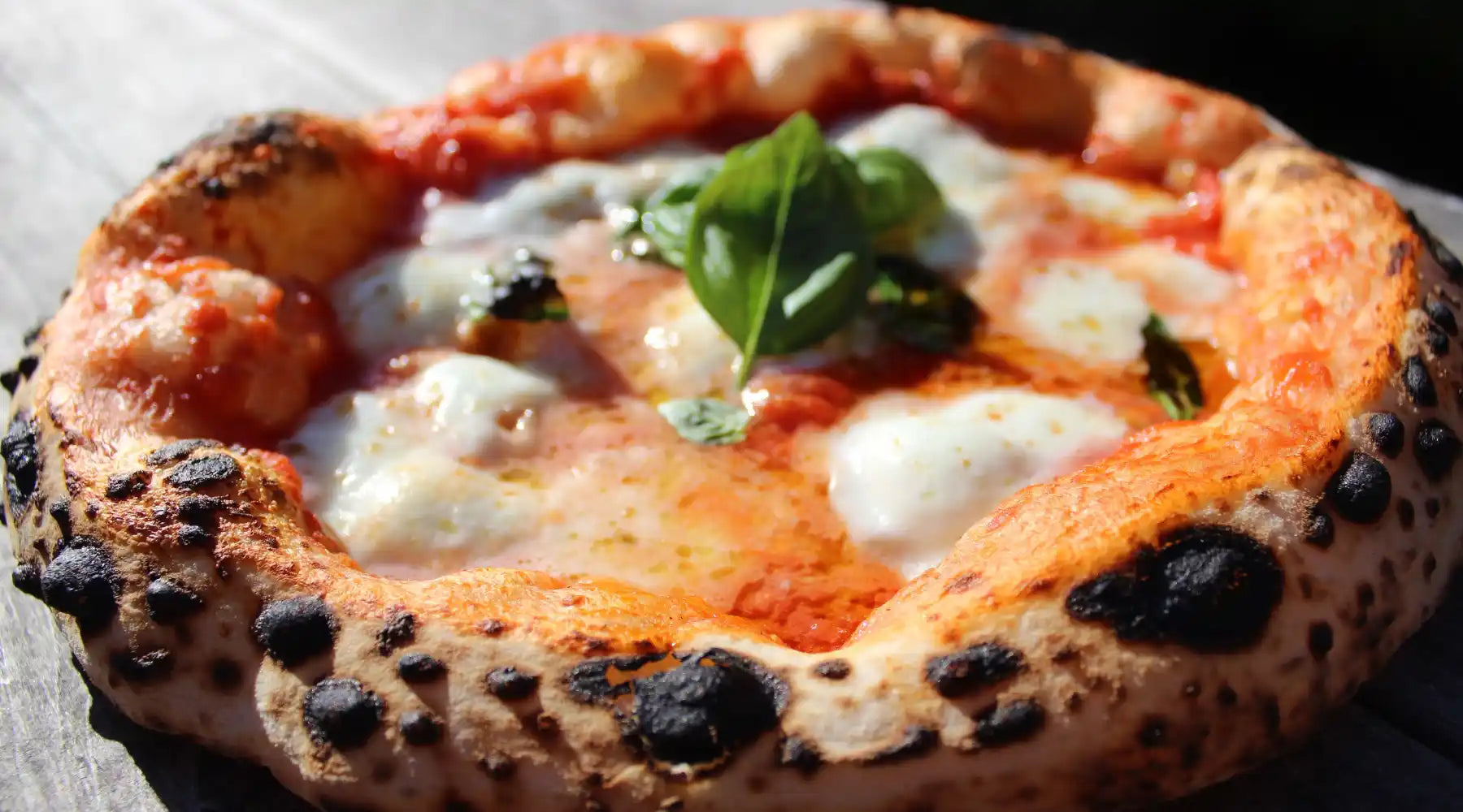 Pizza napolitaine artisanale avec mozzarella fondue, basilic frais et pâte à bord doré.